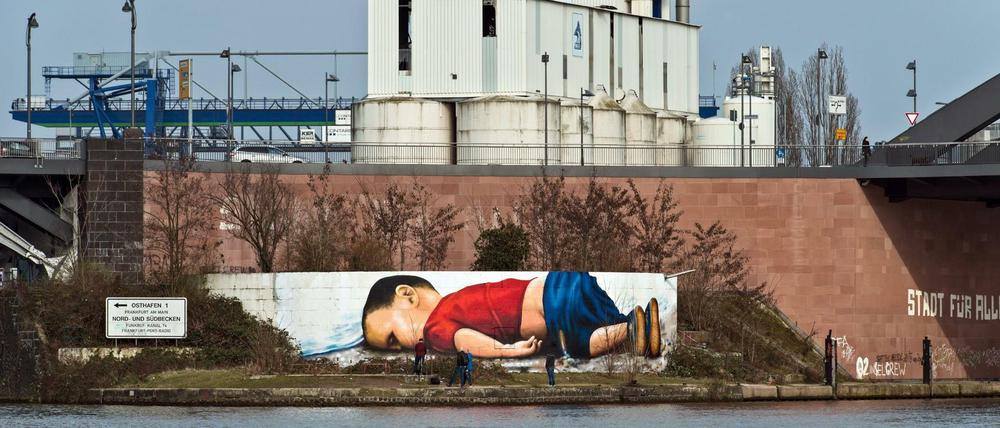 Im September 2015 wurde an der türkischen Kueste ein kleiner syrischer Junge angespüllt - ertrunken auf der Flucht. Jetzt prangt es als Graffito auf einer Mauer am Frankfurter Osthafen, unweit der Europaeischen Zentralbank.