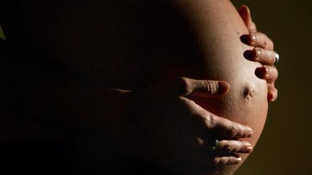 Eine hochschwangere Frau fasst sich mit beiden Händen an ihren Bauch (Archivfoto). 