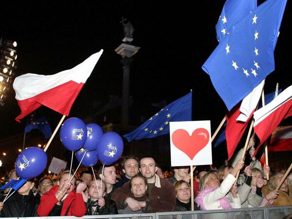Menschen winken mit polnischen und Europafahnen bei den Feiern zum EU-Beitritt auf dem Zamkowy-Platz in Warschau. Feuerwerke, Konzerte und Volksfeste: In ganz Europa haben Millionen Menschen die Erweiterung der EU 2004 gefeiert. 
