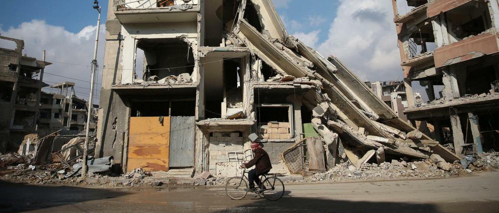 Ein Mann fährt auf einem Fahrrad vor Häuserruinen in der von syrischen Rebellen gehaltenen Stadt Douma. 