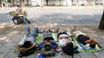 Vier Männer liegen auf einer Decke und schlafen im Hintergrund ein Obst-Straßenverkäufer