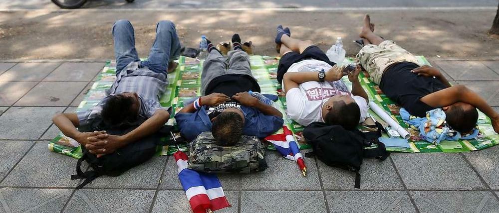 Vier Männer liegen auf einer Decke und schlafen im Hintergrund ein Obst-Straßenverkäufer