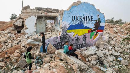 Kinder im syrischen Binnish neben einem Wandgemälde, das aus Solidarität mit der Ukraine an die Wand eines zerstörten Hauses gemalt wurde. Russlands Bombardements haben in Syrien viele Ortschaften zerstört.