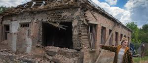 Eine Ukrainerin zeigt auf ihr durch russischen Beschuss schwer beschädigtes Haus.