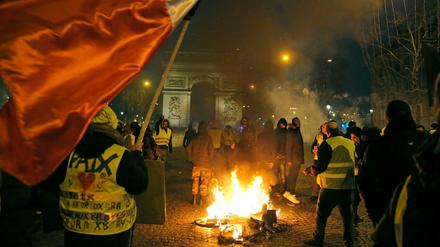 Demonstranten mit gelben Westen stehen neben einem brennenden Fahrrad auf den Champs-Elysées. 