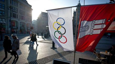 Flaggen mit den Olympischen Ringen und dem Wappen von Hamburg neben einem Straßenkaffee am Rathausmarkt in Hamburg. Die Hansestadt ist bestrebt, mehr Sportveranstaltungen auszurichten.
