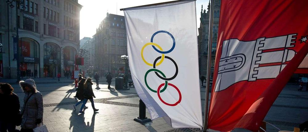 Flaggen mit den Olympischen Ringen und dem Wappen von Hamburg neben einem Straßenkaffee am Rathausmarkt in Hamburg. Die Hansestadt ist bestrebt, mehr Sportveranstaltungen auszurichten.