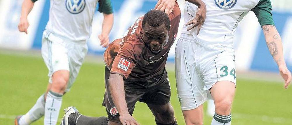 Er spürte ein leichtes Ziehen an der Seite. Gerald Asamoah vom FC St. Pauli (Mitte) sucht den Weg nach vorne, der Wolfsburger Simon Kjaer hält ihn zurück. Foto: dpa