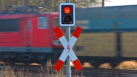 Ein Güterzug passiert einen Bahnübergang, das Signal für den Autoverkehr steht auf Rot. 