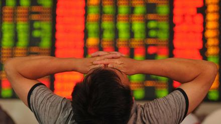 Ein chinesischer Investor vor einer Kurswand schlägt die Hände über dem Kopf zusammen. 
