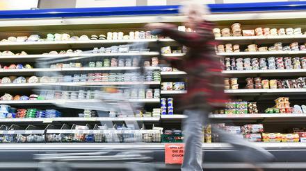 Eine Kundin geht in einem Supermarkt mit ihrem Einkaufswagen an einem Kühlregal vorbei. 