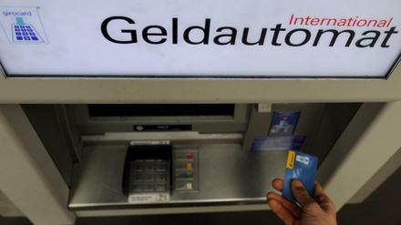 Ein Bankkunde hebt mit seiner Girokarte Bargeld von einem Geldautomaten ab.