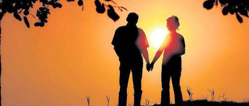 Ein Mann und eine Frau stehen Hand in Hand vor einem Sonnenuntergang.