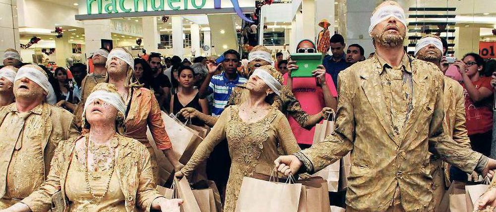 Eine Gruppe von Kunststudenten protestiert in einem Kaufhaus in Brasilien gegen Konsumverzicht. Sie sind mit brauner Farbe beschmiert und tragen braune Papiertüten.