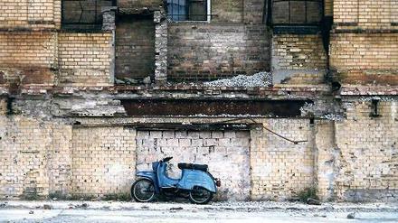 Ein blauer Simson-Motorroller steht vor einer Ruine.