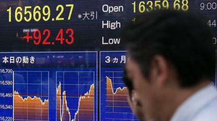 Ein Passant läuft am Freitag an Bildschirmen der Tokioter Börse vorbei. In Japan haben rote Ziffern eine positive Bedeutung.