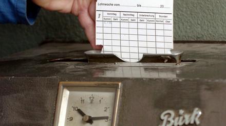 Eine Hand steckt eine Karte in ein Arbeitszeiterfassungsgerät, eine so genannte Stechuhr.