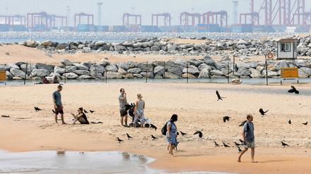 Zwischen Tourismus und Handel. Urlauber spazieren am Strand von Colombo in Sri Lanka, während im Hintergrund an der großen Hafen-City gebaut wird.