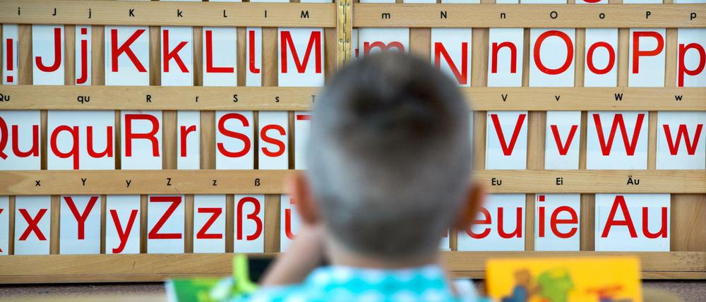 Ein kleines Kind sitzt vor einem Wandbord, in dem einzelne Buchstaben in Groß- und Kleinschreibung aufgereiht sind.