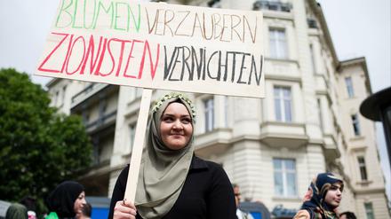 Eine Frau hält ein Plakat mit der Aufschrift "Blumen verzaubern, Zionisten vernichten" hoch.