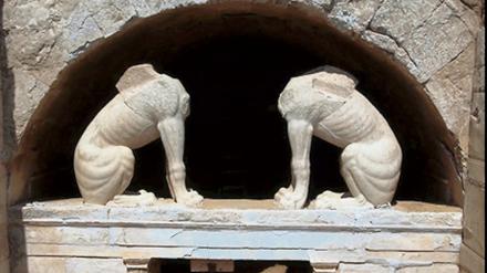 Zwei kopflose Sphinxen stehen in einer Ausgrabungsstätte unter einem Torbogen auf einem Sockel.