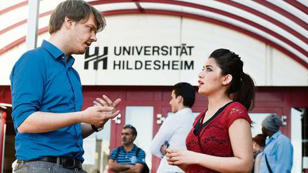 Ein Juniorprofessor und eine Studentin stehen vor der Universität Hildesheim und sprechen miteinander.