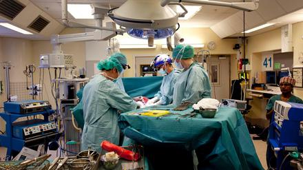 Männer in blau-grünen Kitteln stehen an einem Operationstisch.
