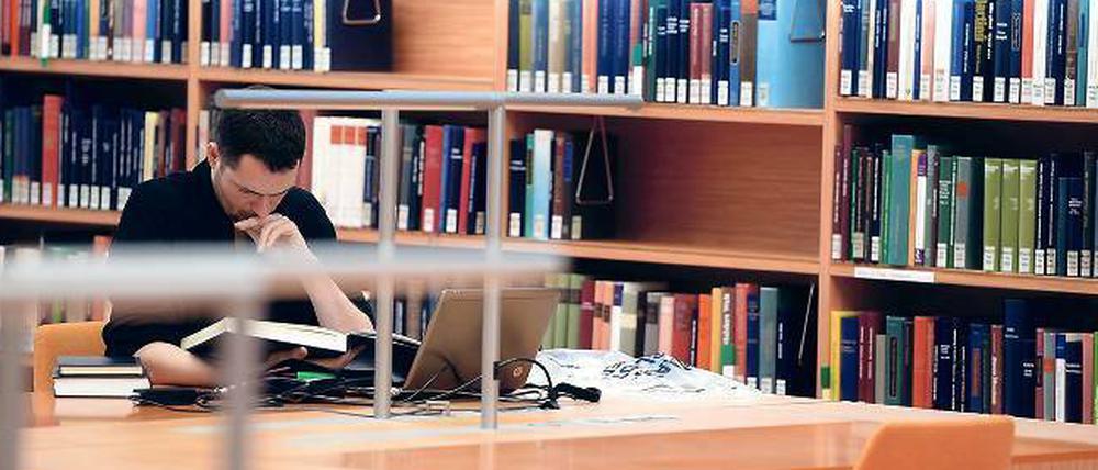 Ein Wissenschaftler mit Laptop und Buch in der Bibliothek.