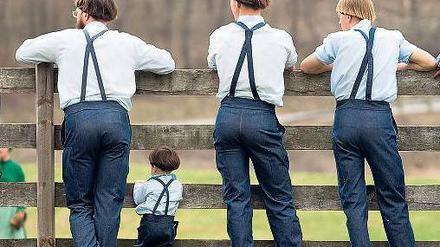 Drei erwachsene Amish und ein Kind stehen mit dem Rücken zum Betrachter an einem Zaun.