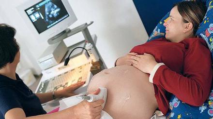 Der Bauch einer Schwangeren wird mit Ultraschall unetrsucht. Die Umrisse des Kindes sind auf dem Bildschirm an der Wand zu erkennen.