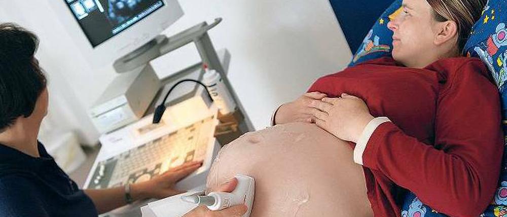 Der Bauch einer Schwangeren wird mit Ultraschall unetrsucht. Die Umrisse des Kindes sind auf dem Bildschirm an der Wand zu erkennen.