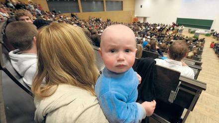 Eine junge Frau steht mit einem Kleinkind auf dem Arm in einem Hörsaal.