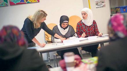 Junge Frauen mit Kopftüchern sitzen an Tischen in einem Klassenzimmer, eine andere Frau erklärt ihnen etwas.