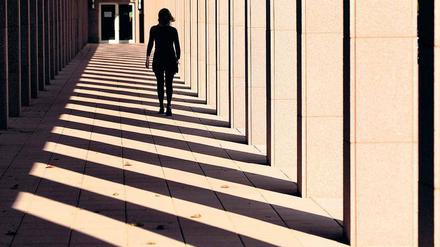 Eine Frau, die an einem Gebäude entlang geht, ist von hinten als Silhouette zu sehen.