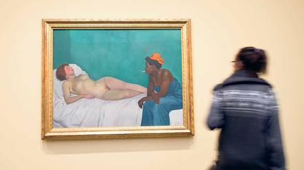 Eine Frau steht vor einem Gemälde, das eine schwarze Frau beim Betrachten einer weißen, schlafenden Frau zeigt.