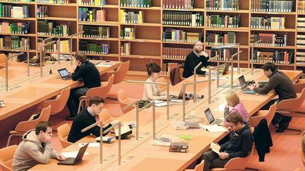 Junge Männer und Frauen sitzen in einer Bibliothek, lesen und arbeiten an ihren Laptops.
