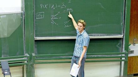 Ein junger Mann steht in einem Hörsaal vor einer Tafel und erklärt Formeln.