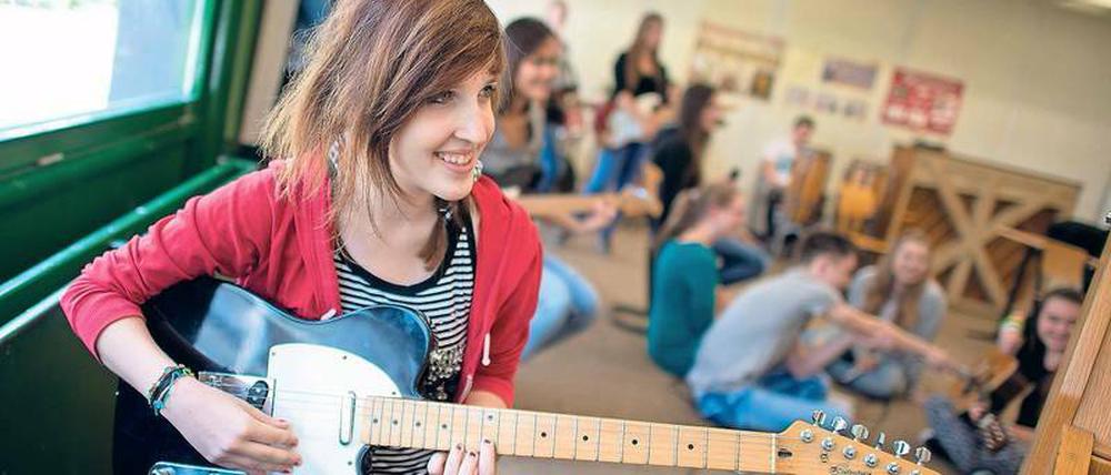 Eine junge Frau sitzt in einem Klassenzimmer und spielt Gitarre.