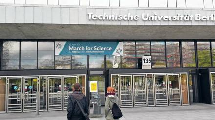 Zwei Studierende stehen vor der TU Berlin und blicken auf ein Plakat, das zum Science March aufruft.