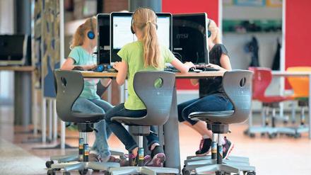 Drei Mädchen sitzen auf Bürostühlen an einem runden Tisch und arbeiten an Computern.