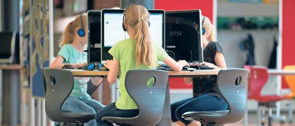 Drei Mädchen sitzen auf Bürostühlen an einem runden Tisch und arbeiten an Computern.