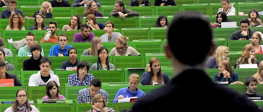 Ein junger Professor steht vor Studierenden im Hörsaal.