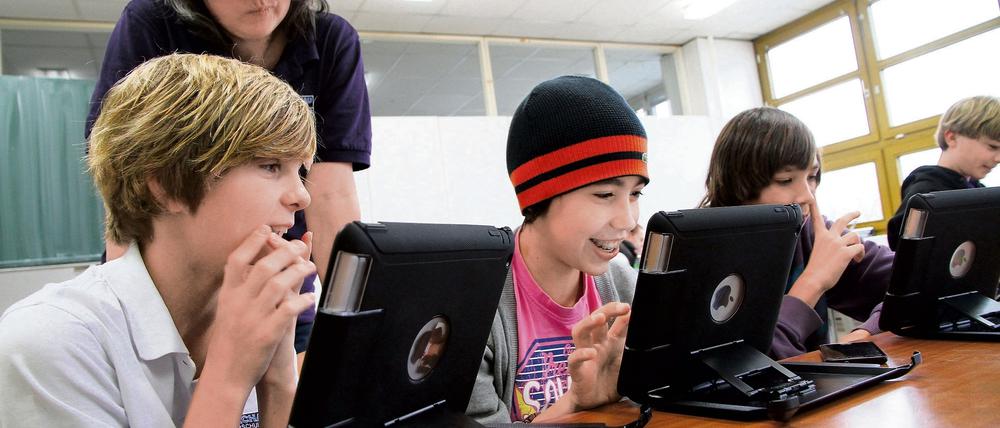 Schüler sitzen in einem Klassenraum vor Tablet-Computern, sie lächeln dabei.