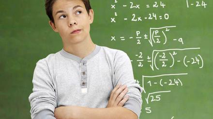Ein Junge steht vor einer mit Matheaufgaben beschriebenen Tafel.