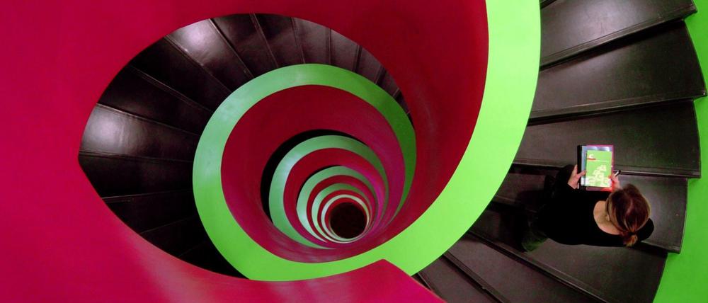 Eine Frau geht auf einer zweifarbig gestalteten Wendeltreppe nach oben.