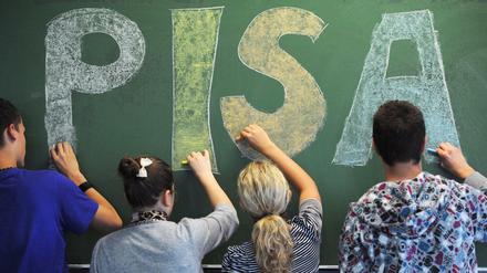 Vier Schüler stehen an einer Tafel und schreiben den Schriftzug "Pisa".