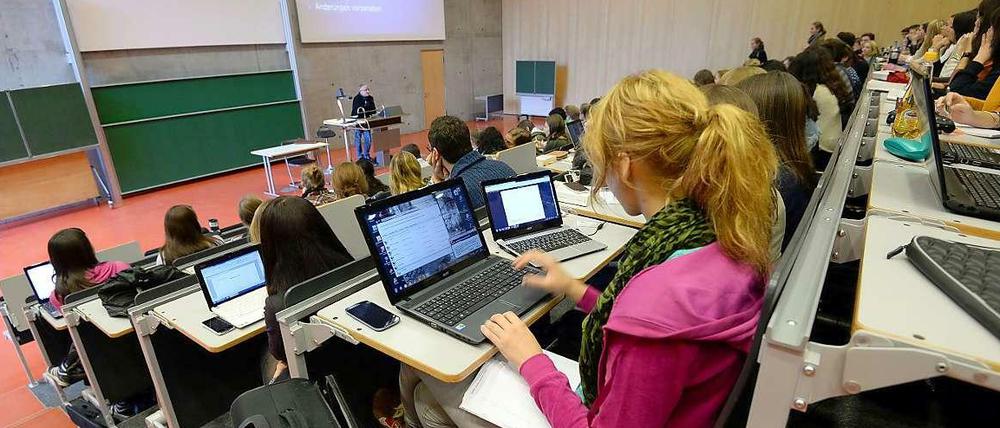 Studierende sitzen in einem Hörsaal, ein Professor steht an einem Stehpult und zeigt eine Powerpointpräsentation.