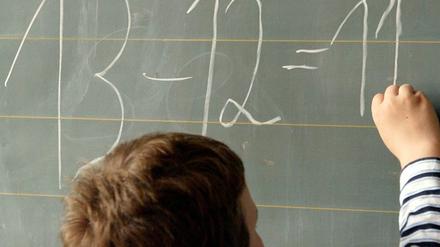 Ein Junge schreibt eine einfache Gleichung an die Tafel.