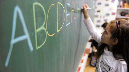Ein Mädchen schreibt das ABC mit farbiger Kreide in Großbuchstaben auf eine Tafel.