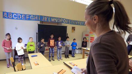 In einem Klassenraum steht eine Lehrerin vor einer Gruppe von Schülern.